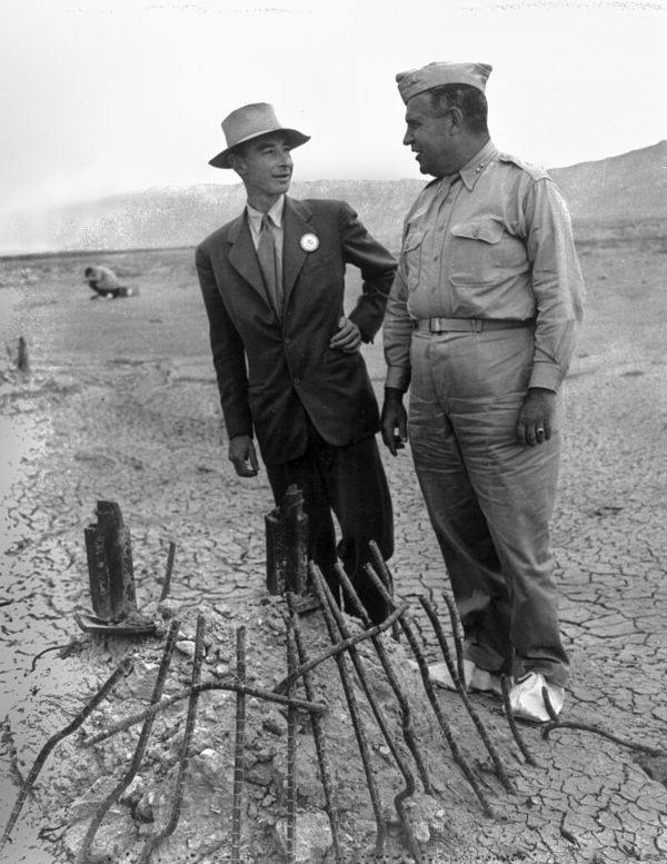Nhà vật lý Oppenheimer (bên trái) và Thiếu tướng Leslie Groves tại tàn tích của cuộc thử nghiệm Trinity ở New Mexico vào tháng 09/1945. Những đôi giày được bọc vải bạt màu trắng bên ngoài, ngăn bụi phóng xạ bám vào đế giày của họ. Công binh Lục quân Hoa Kỳ. (Ảnh: Tư liệu công cộng)