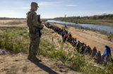 Một người lính thuộc Lực lượng Vệ binh Quốc gia Texas trông chừng một nhóm hơn 1,000 người nhập cư đã vượt sông Rio Grande từ Mexico ở Eagle Pass, Texas, hôm 18/12/2023. (Ảnh: John Moore/Getty Images)