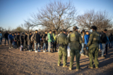 Một nhóm người nhập cư bất hợp pháp được Lực lượng Tuần tra Biên giới tiến hành giải quyết thủ tục sau khi vượt sông gần xa lộ bên ngoài Eagle Pass, Texas, hôm 04/02/2024. (Ảnh: Sergio Flores/AFP/Getty Images)