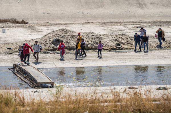 Người di cư băng qua sông Tijuana và tiến về bức tường biên giới Hoa Kỳ ở Tijuana, Mexico, hôm 11/05/2023. (Ảnh: John Fredricks/The Epoch Times)