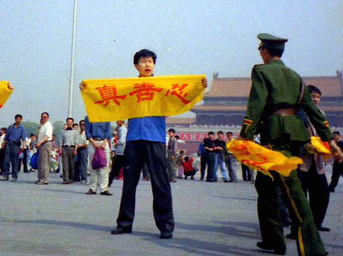 Một viên công an Trung Quốc tiến đến gần một học viên Pháp Luân Công tại Quảng trường Thiên An Môn ở Bắc Kinh khi anh cầm tấm biểu ngữ có các Hán tự “chân, thiện, nhẫn,” những nguyên lý cốt lõi của Pháp Luân Công. (Ảnh: Đăng dưới sự cho phép của Minghui.org)