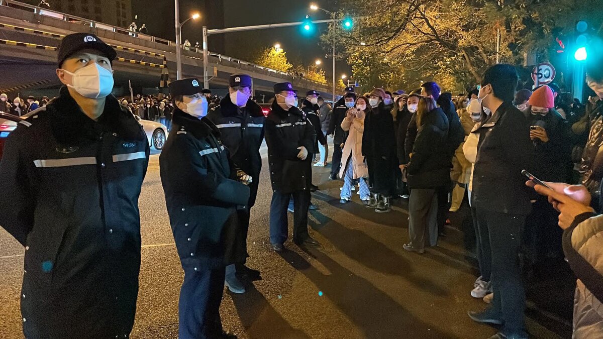 Cảnh sát theo dõi những người biểu tình tụ tập dọc đường phố trong cuộc biểu tình tưởng nhớ các nạn nhân của vụ hỏa hoạn tang thương cũng như cuộc biểu tình phản đối các biện pháp chống dịch COVID-19 hà khắc của Trung Quốc tại Bắc Kinh vào ngày 28/11/2022. (Ảnh: Michael Zhang/AFP qua Getty Images)