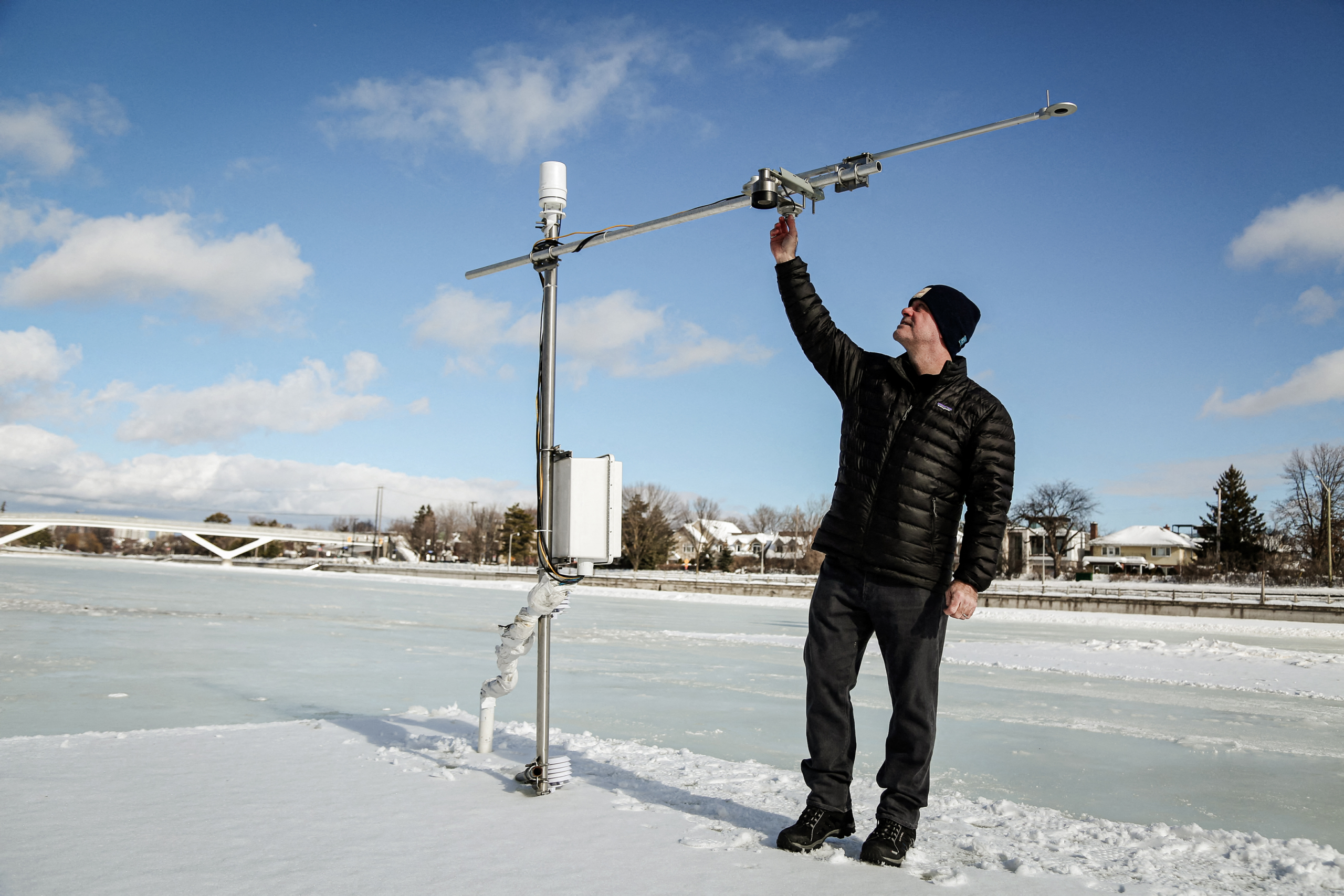 (Phía trên) Giáo sư dọn tuyết xung quanh trạm thời tiết. (Phía dưới) Một giáo sư kỹ thuật dân dụng và môi trường điều chỉnh trạm thời tiết thu nhỏ được thiết lập trên Kênh Rideau ở Ottawa, Canada, ngày 08/02/2023. (Ảnh: Dave Chan/AFP qua Getty Images)