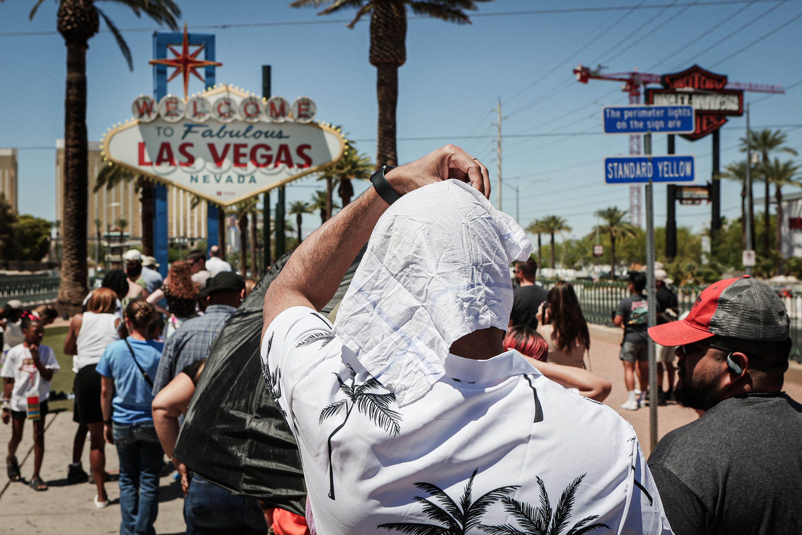 (Trên) Một người đàn ông đi ngang qua vòi phun nước trong một ngày nắng nóng ở Tokyo, vào ngày 29/07/2022. (Dưới) Một người đàn ông che nắng khi xếp hàng chờ chụp ảnh tại biển hiệu có dòng chữ Chào mừng đến Las Vegas, một biển hiệu mang tính lịch sử, trong một đợt nắng nóng ở Las Vegas, vào ngày 14/07/2023. (Ảnh: Philip Fong/AFP qua Getty Images, Ronda Churchill/AFP qua Getty Images)