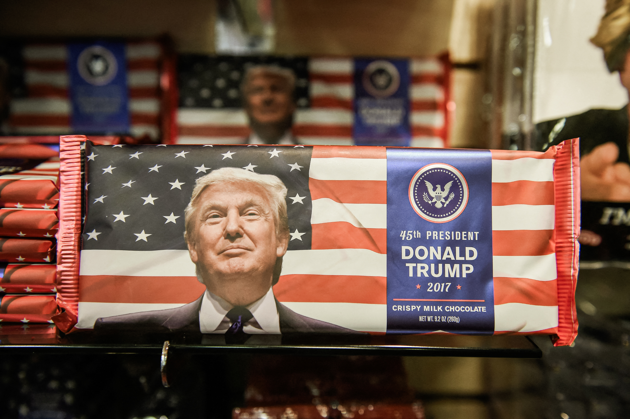 (Ảnh trên) Hàng hóa mang thương hiệu Trump được trưng bày tại một cửa hàng trong Trump Tower ở Thành phố New York, vào ngày 04/01/2022. (Ảnh dưới) Những thanh sô cô la mang thương hiệu Donald Trump được bán trong một cửa hàng quà tặng một ngày trước ngày nhậm chức của ông Trump ở Hoa Thịnh Đốn, vào ngày 19/01/2017. (Ảnh: Spencer Platt/Getty Images, Robyn Beck/AFP qua Getty Images)