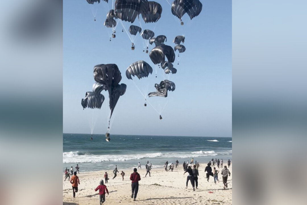 Người dân Palestine chạy về phía những chiếc dù gắn với các gói thực phẩm được thả từ những chiếc phi cơ của Hoa Kỳ xuống một bãi biển, ở Dải Gaza, hôm 02/03/2024. (Ảnh: AFP qua Getty Images)