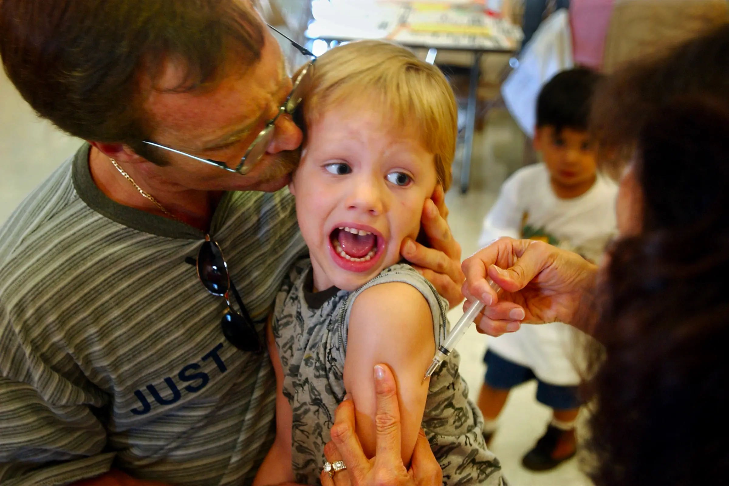 Học sinh mẫu giáo Jeremy Conner, 5 tuổi, phản ứng khi được chích vaccine MMR và cha cậu là anh Mark Conner cố gắng an ủi con. Ảnh được chụp tại Santa Ana, California hôm 26/08/2002. (Ảnh: David McNew/Getty Images)