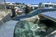 Mọi người đang xem những chiếc xe hơi bị hư hỏng trong một bãi đậu xe của nhân viên ở phi trường sau khi mảnh lốp từ một chiếc Boeing 777 hạ cánh tại Phi trường Quốc tế San Francisco, hôm 07/03/2024. (Ảnh: Haven Daley/AP Photo)