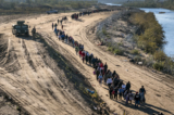 Một bức ảnh chụp từ trên không cho thấy một nhóm gồm hơn 1,000 người nhập cư đi về phía trung tâm giải quyết thủ tục tại hiện trường của Đội Tuần tra Biên giới Hoa Kỳ sau khi họ vượt sông Rio Grande từ Mexico ở Eagle Pass, Texas, vào ngày 18/12/2023. (Ảnh: John Moore/Getty Images)
