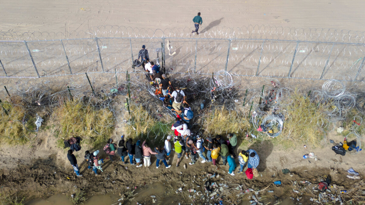 Những người nhập cư bất hợp pháp vượt hàng rào dây thép gai khi băng qua biên giới Hoa Kỳ-Mexico ở El Paso, Texas, hôm 13/03/2024. (Ảnh: John Moore/Getty Images)