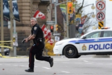 Một viên cảnh sát đang chạy cùng với khẩu súng trên tay ở Ottawa vào ngày 22/10/2014, trong một vụ tấn công của ông Michael Zehaf Bibeau vào Parliament Hill. Ông Bibeau đã bắn Hạ sĩ Nathan Cirillo và làm bị thương một nhân viên bảo an trước khi bị trung sĩ của Nghị viện bắn hạ. (Ảnh: The Canadian Press/Sean Kilpatrick)