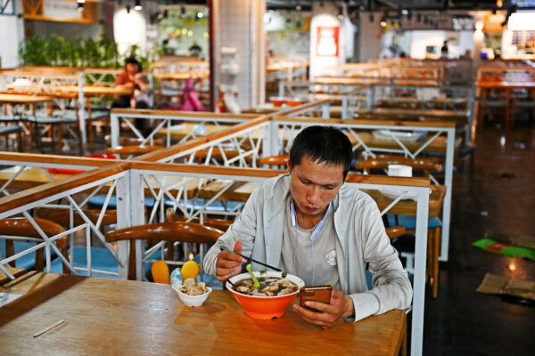 Một người đàn ông kiểm tra điện thoại trong lúc đang ăn tại một khu ẩm thực ở một trung tâm mua sắm tại Bắc Kinh hôm 15/08/2023. Chứng khoán toàn cầu đã sụt giảm hôm 15/08 sau khi dữ liệu đáng thất vọng từ Trung Quốc làm gia tăng lo ngại về tình trạng của nền kinh tế lớn thứ hai thế giới. (Ảnh: Greg Baker/AFP qua Getty Images)