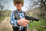 Chủ trang trại chăn nuôi gia súc Jim Chilton cho xem khẩu súng lục cỡ nòng 40 mà ông mang theo khi ra ngoài tại trang trại rộng 50,000 mẫu Anh của mình ở Arivaca, Arizona, hôm 22/03/2024. (Ảnh: Allan Stein/The Epoch Times)