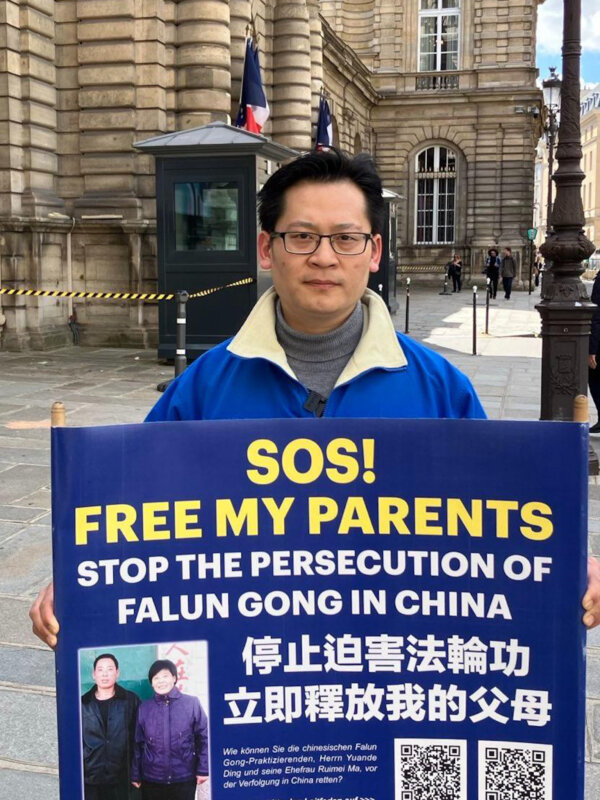 Học viên Pháp Luân Công Đinh Nhạc Bân (Ding Lebin) cầm một tấm biển kêu gọi sự chú ý của cộng đồng quốc tế về cuộc đàn áp đối với gia đình anh vì kiên định với môn tu luyện này ở Trung Quốc, cạnh Cung điện Luxembourg ở Paris, hôm 06/05/2024. (Ảnh: David Vives/NTD)