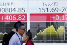 Người dân đi ngang qua một bảng điện tử hiển thị giá cổ phiếu thuộc chỉ số Nikkei của Sở Giao dịch Chứng khoán Tokyo (trái) và tỷ giá đồng yên Nhật so với USD (phải) dọc một con phố ở Tokyo hôm 27/03/2024. (Ảnh: Kazuhiro Nogi/AFP qua Getty Images)