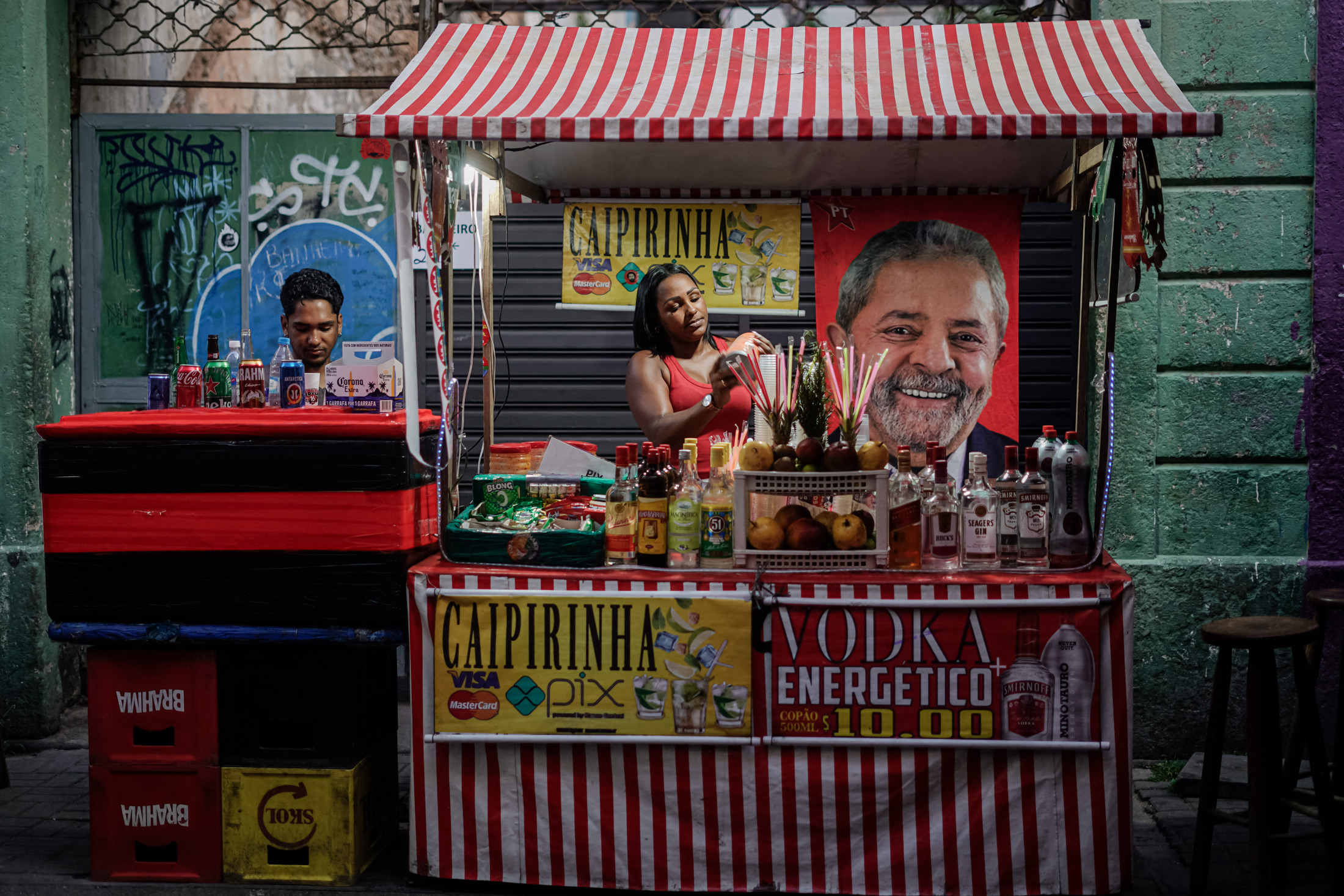 Một người ủng hộ ứng cử viên tổng thống Brazil Luiz Inácio Lula da Silva treo lá cờ có ảnh của ứng cử viên này trên quầy hàng trên đường phố của cô trong cuộc bầu cử tổng thống sắp diễn ra, ở Rio de Janeiro ngày 30/10/2022. Kể từ khi Tổng thống Lula nhậm chức, chính phủ của ông đã phải chật vật để giải quyết lạm phát và tỷ lệ thất nghiệp cao. (Ảnh: Mauro Pimentel/AFP qua Getty Images)