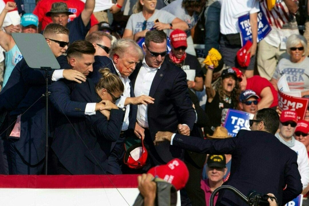 Cựu Tổng thống Donald Trump, ứng cử viên bên Đảng Cộng Hòa, với vết máu trên mặt, đang được các nhân viên mật vụ vây quanh trong khi hộ tống ông ra khỏi sân khấu tại một sự kiện tranh cử ở Butler Farm Show Inc. tại Butler, Pennsylvania, hôm 13/07/2024. (Ảnh: Rebecca Droke/ AFP qua Getty Images)