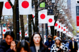 Người dân đi bộ ngang qua một hàng quốc kỳ Nhật Bản tại một khu mua sắm ở Tokyo hôm 19/03/2024. (Ảnh: Kim Kyung-Hoon/Reuters)