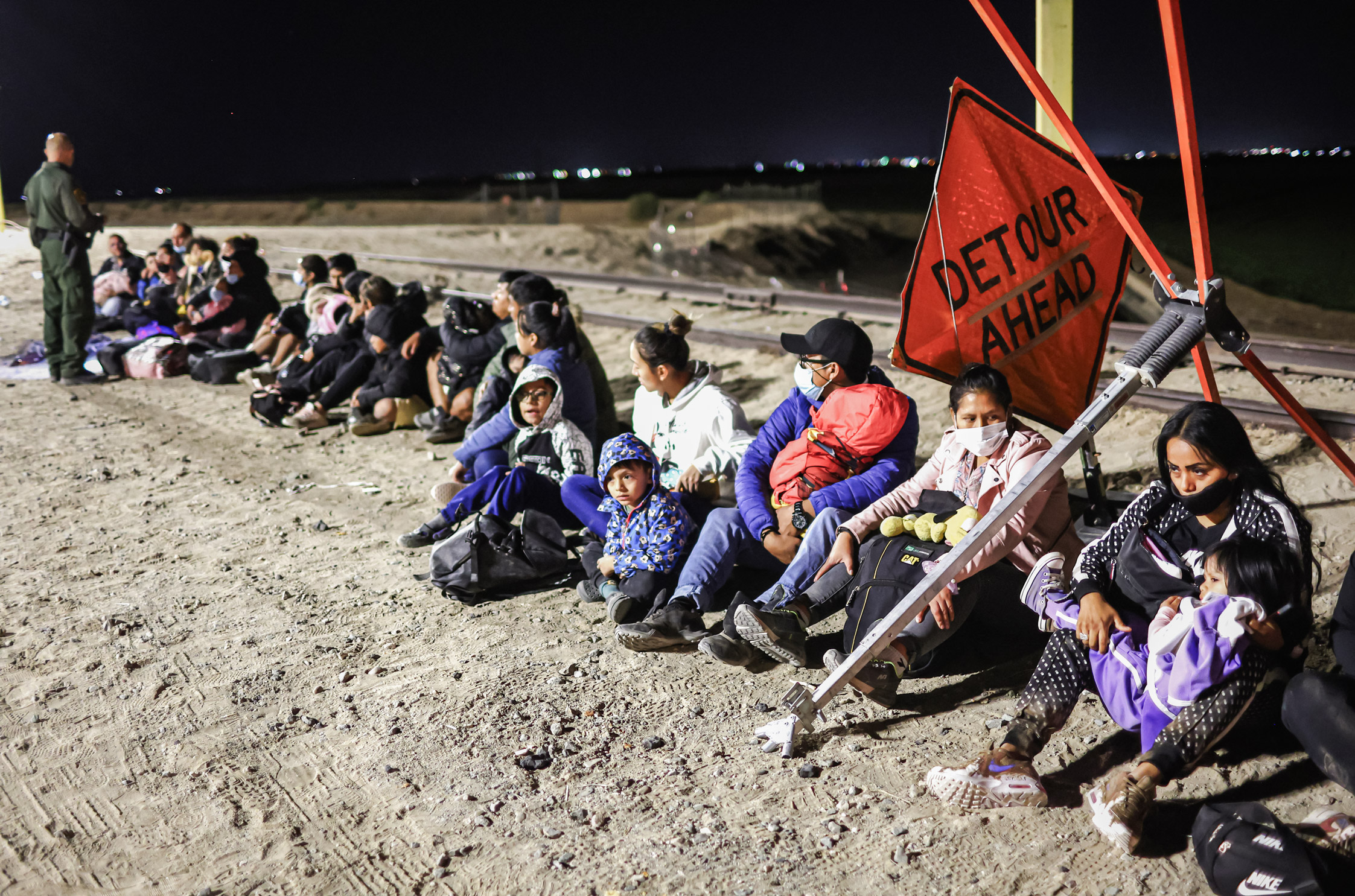 Những người nhập cư bất hợp pháp chờ để được các nhân viên Tuần tra Biên giới giải quyết thủ tục sau khi vượt biên từ Mexico, đằng sau là hàng rào biên giới Hoa Kỳ-Mexico, ở Yuma, Arizona, ngày 23/05/2022. (Ảnh: Mario Tama/Getty Images)